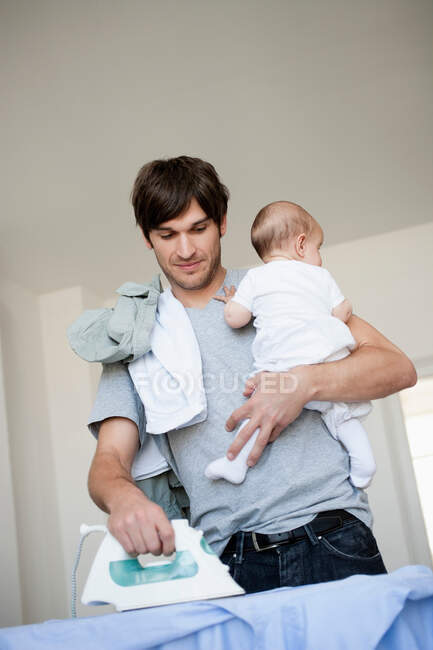 Vater mit Baby im Arm bügelt — Stockfoto