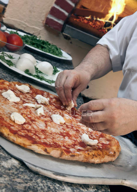 Abgeschnittenes Bild vom Koch, der Pizza mit Käse garniert — Stockfoto