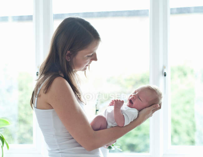 Mother holding infant son by window — Stock Photo