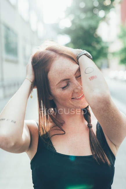 Молодая женщина с длинными рыжими волосами и веснушками с закрытыми глазами на городской улице — стоковое фото