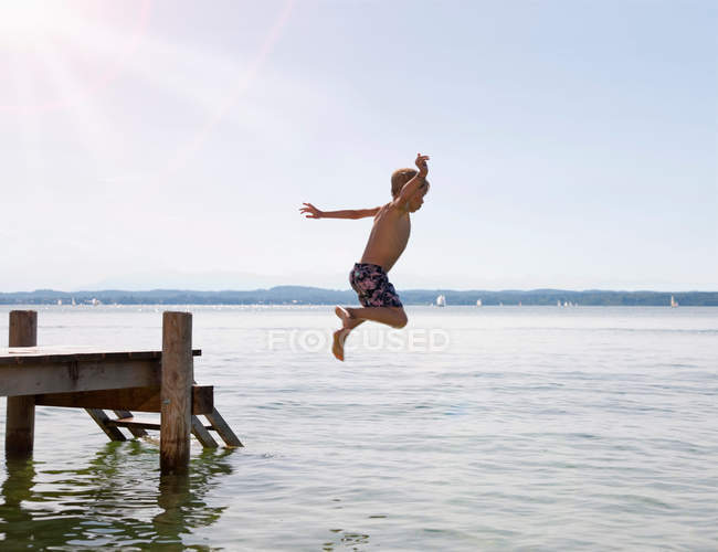 Ragazzo che salta nel lago dal molo — Foto stock