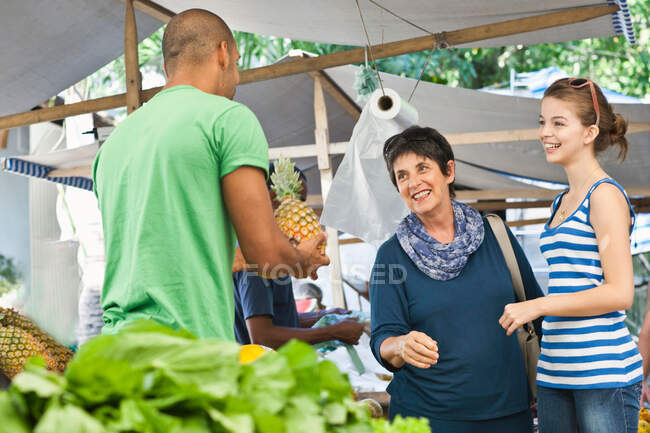 Uomo che vende ananas alle donne sul mercato — Foto stock