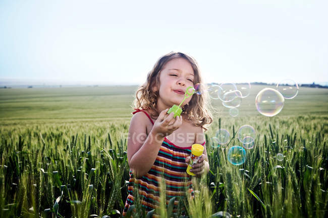 Girl blowing bubbles in wheat field — Stock Photo
