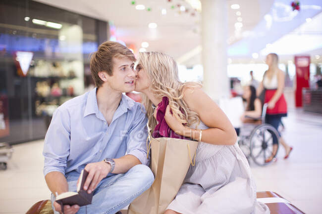Молодая женщина целует мужчину в щёку в торговом центре — стоковое фото