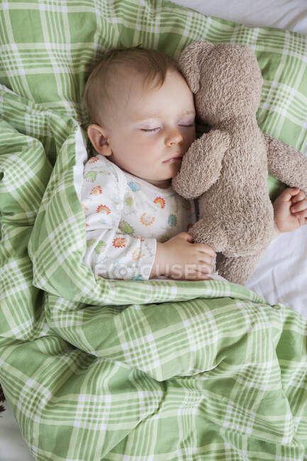 Overhead view of baby boy asleep on bed holding teddy bear — Stock Photo