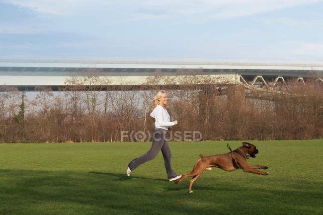 Mulher correndo com cão no campo — Fotografia de Stock