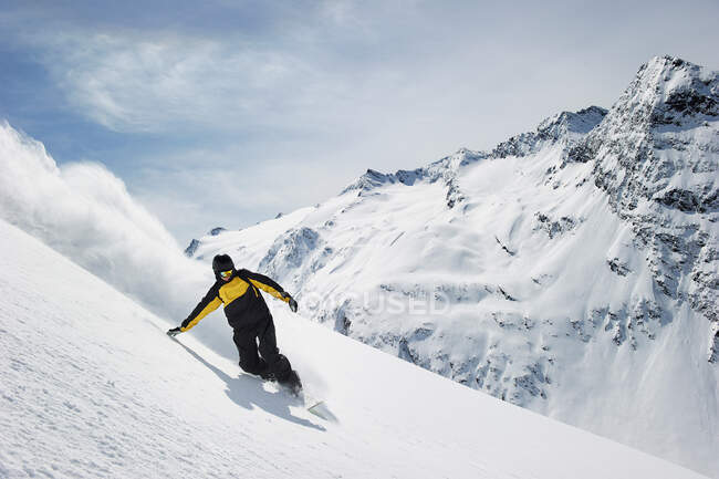 Man snowboarding on snow caped mountain descent — Stock Photo
