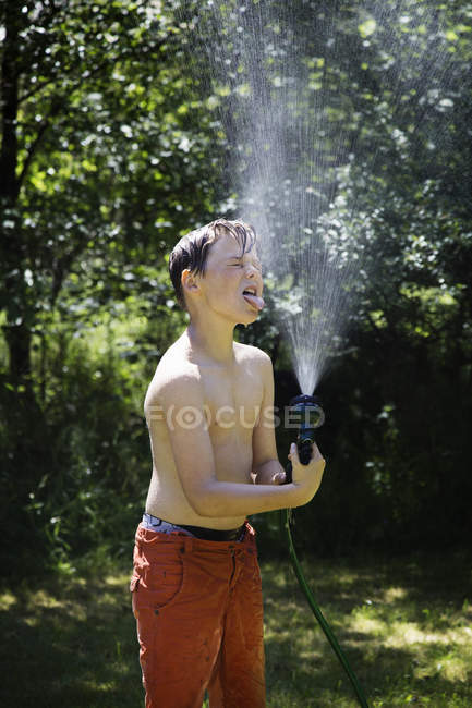Niño jugando con manguera de jardín y agua al aire libre - foto de stock