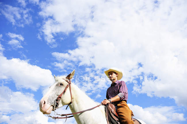 Low angle portrait of young man in cowboy gear riding  horse — Stock Photo