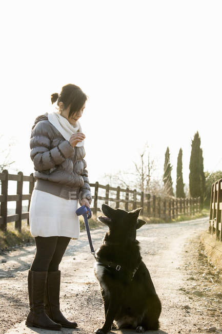 Mid adult woman obedience training her dog on rural road — Stock Photo