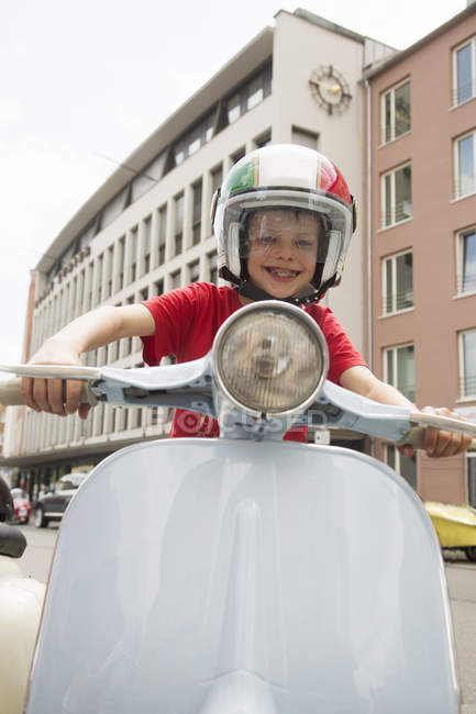 Portrait of ten year old boy pretending to ride motor scooter on city street — Stock Photo