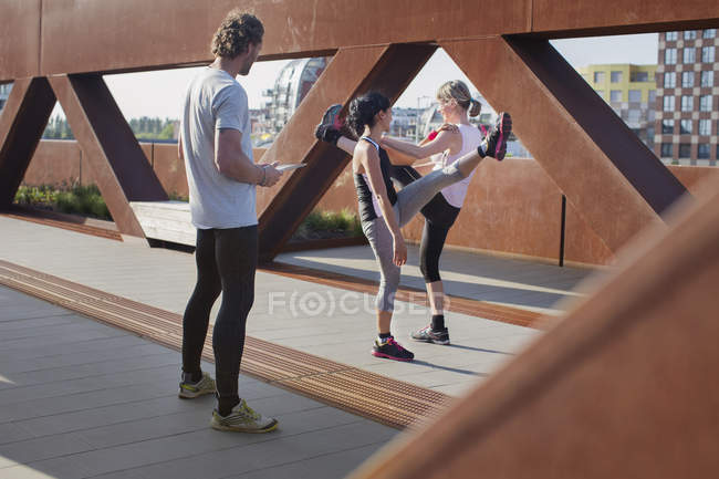 Дві жінки тренуються на міському пішохідному мосту з чоловічим особистим тренером — стокове фото