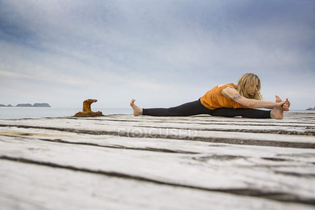 Femme adulte moyenne pratiquant le yoga sur jetée de mer en bois — Photo de stock