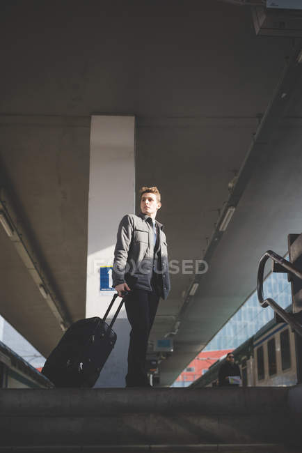 Portrait of young businessman commuter at top of stairs pulling suitcase. — Stock Photo