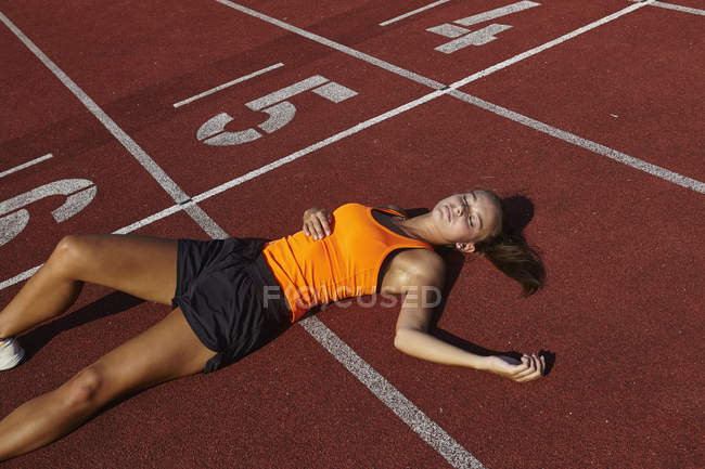 Jovem corredora deitada de costas exausta na pista de corrida — Fotografia de Stock