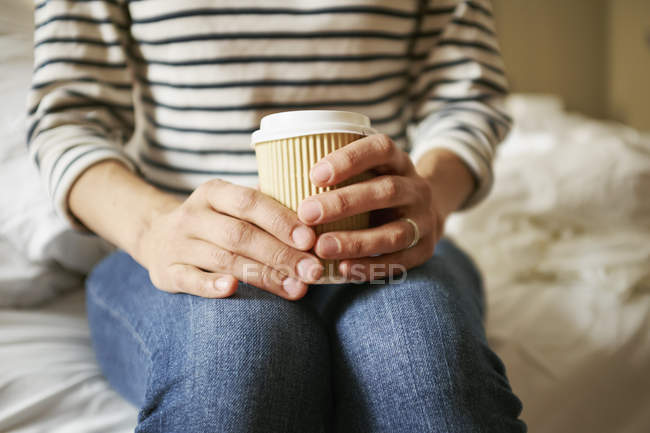 Female hands holding takeaway coffee on bed — Stock Photo