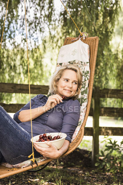 Donna matura rilassante con ciotola di ciliegie su amaca — Foto stock