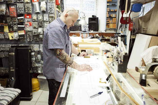 Guitar maker measuring up blueprint design on drawing table — Stock Photo