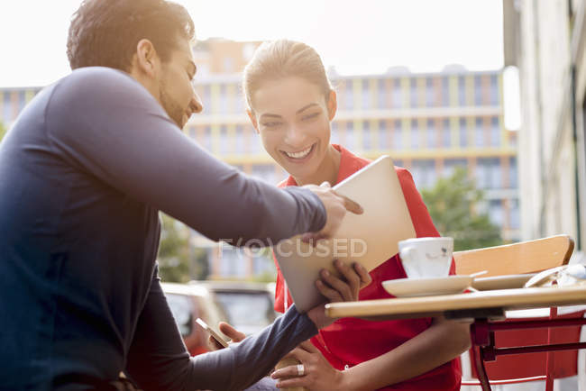 Young man and woman sitting outside cafe, looking at digital tablet — Stock Photo