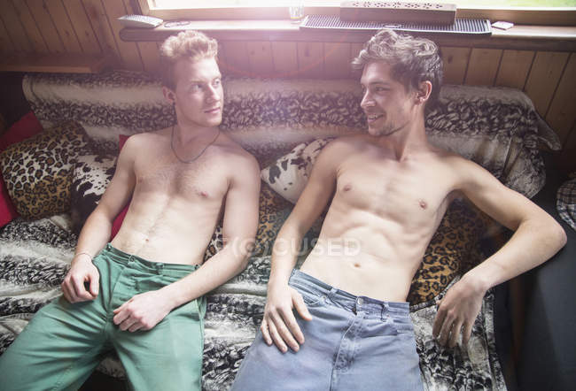 Two young men lying bare chested on bed — Stock Photo