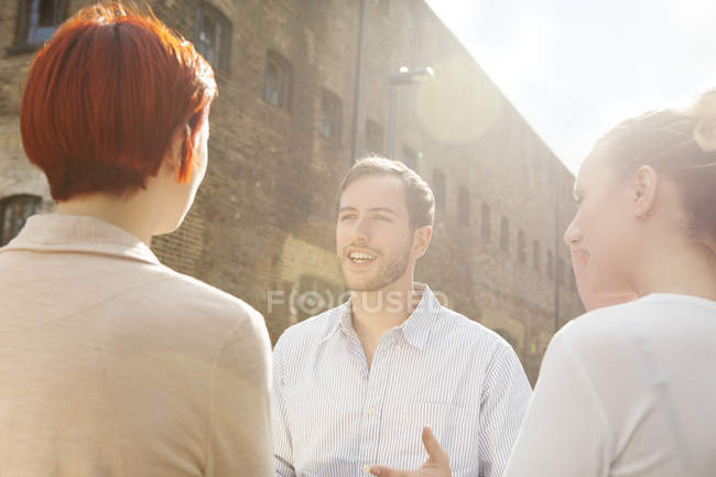Three young people talking by building in city — Stock Photo