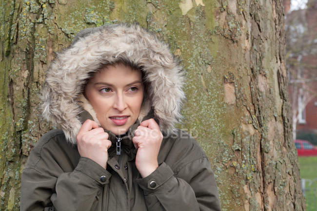 Giovane donna davanti all'albero del parco avvolta nella cappa di pelliccia — Foto stock