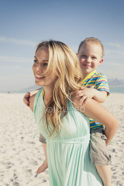 Мати дає молодого сина на свинарство назад на пляжі — стокове фото