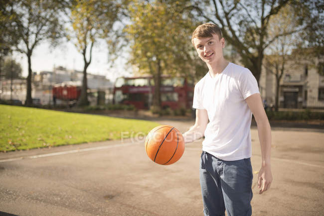 Retrato de un joven jugador de baloncesto sonriente sosteniendo baloncesto - foto de stock