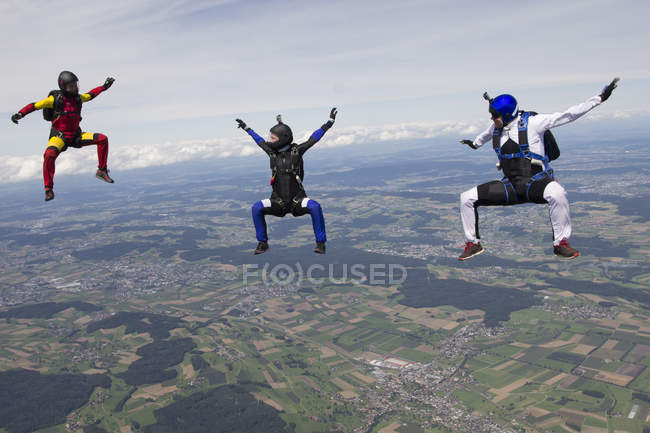 Equipo de tres paracaidistas en posición sit fly sobre Buttwil, Luzern, Suiza - foto de stock
