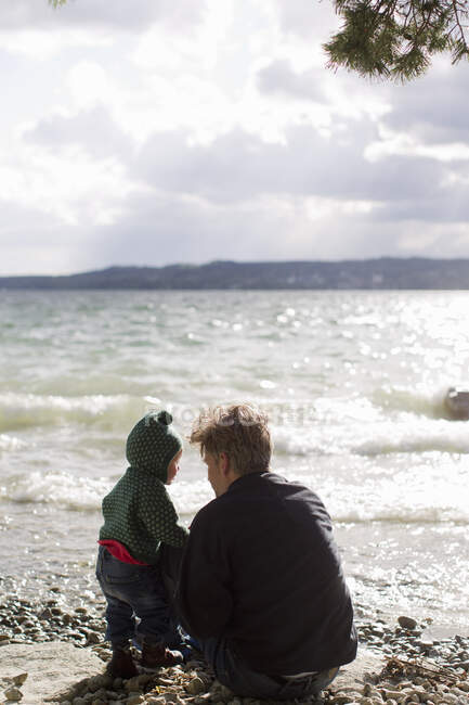 Отец и дочка приседают на берегу озера Штарнберг, Бавария, Германия — стоковое фото
