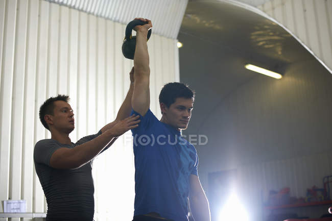 Trainer coaching man with kettlebell in gym — Stock Photo