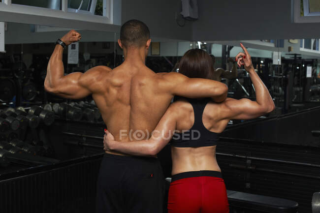 Young woman and mid adult man, flexing muscles, rear view — Stock Photo