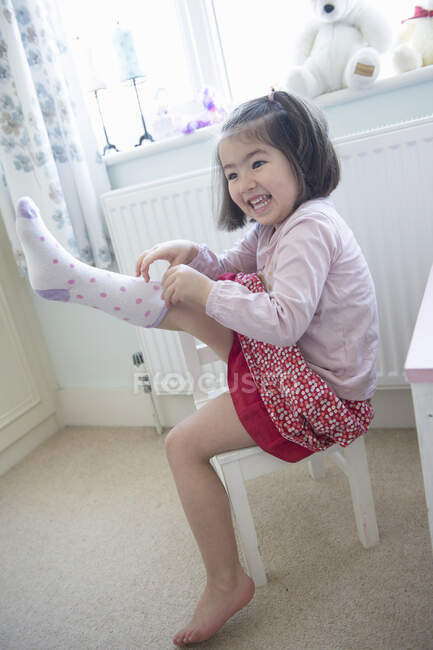 Giovane ragazza seduta sulla sedia, tirando calzino — Foto stock