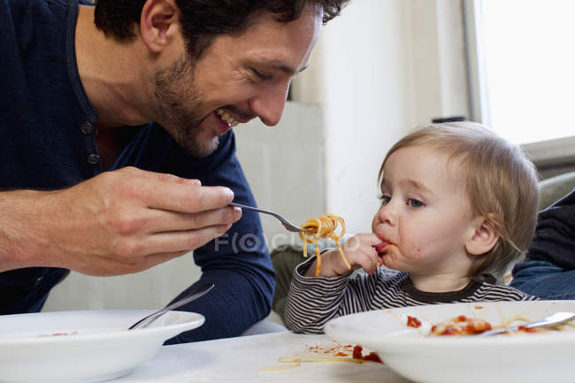 Father feeding toddler daughter spaghetti — Stock Photo