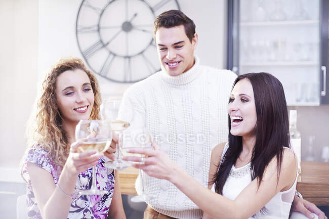 Three young adult friends making a white wine toast in kitchen — Stock Photo