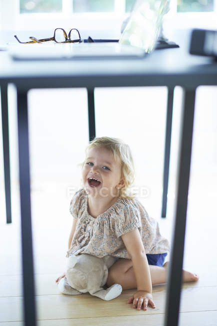 Female toddler hiding and laughing under dining room table — Stock Photo