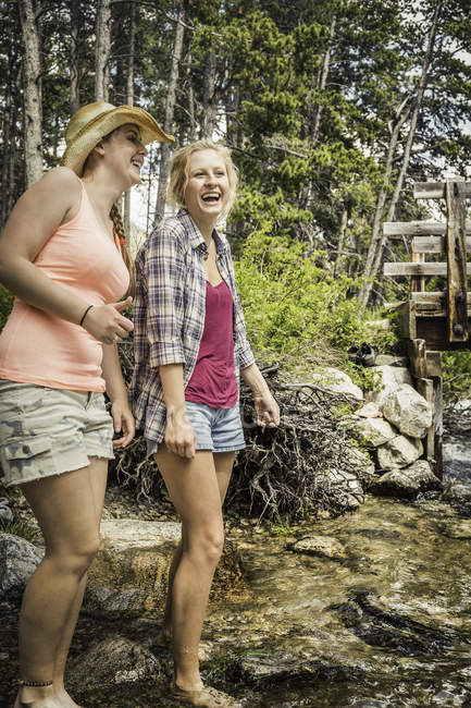 Young woman and teenage girl paddling in forest river, Red Lodge, Montana, USA — Stock Photo