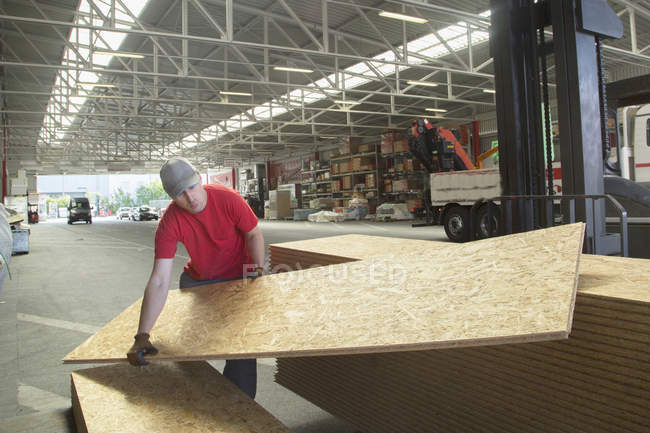 Ouvrier d'entrepôt soulevant des planches en bois dans un entrepôt de quincaillerie — Photo de stock