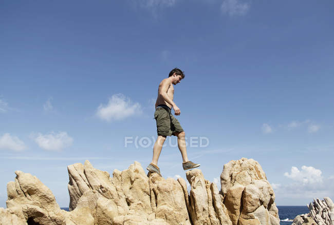 Vista lateral de ángulo bajo del joven escalando sobre rocas, Costa Paradiso, Cerdeña, Italia - foto de stock