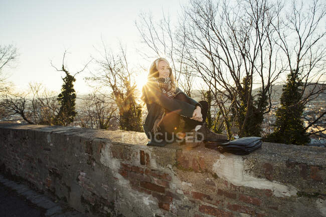 Взрослая женщина, сидящая на стене под солнцем — стоковое фото