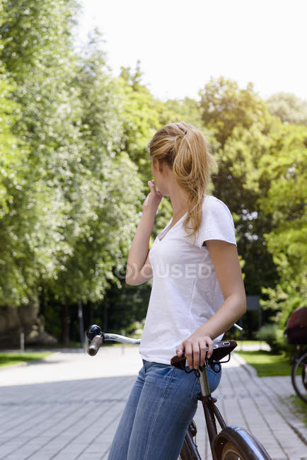 Mujer joven con cola de caballo apoyado contra la bicicleta mirando hacia otro lado - foto de stock