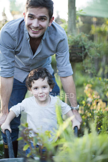 Portrait of mid adult man and son pushing wheelbarrow in allotment — Stock Photo