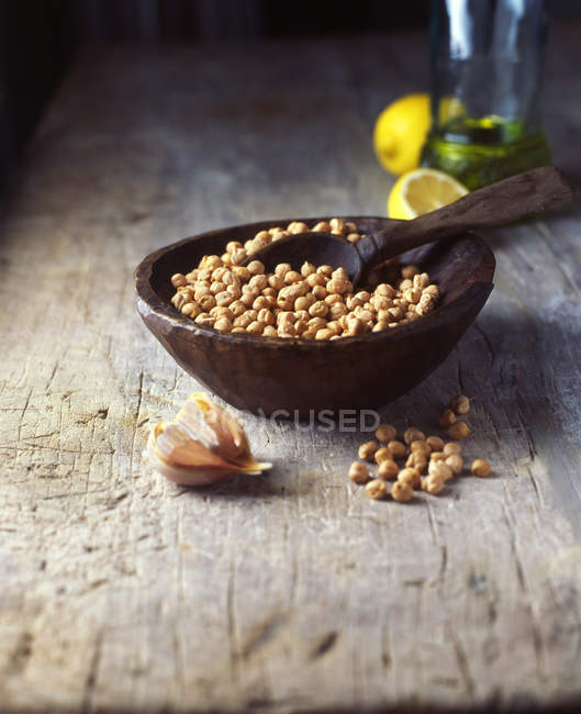 Vintage bowl and wooden spoon with raw chick peas and garlic cloves — Stock Photo