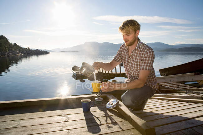 Man making coffee on jetty by sea — Stock Photo