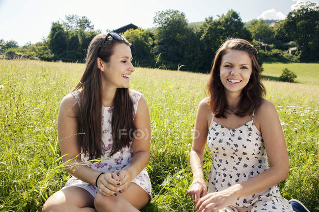 Giovani allegre donne sorridenti sedute in campo con erba verde — Foto stock