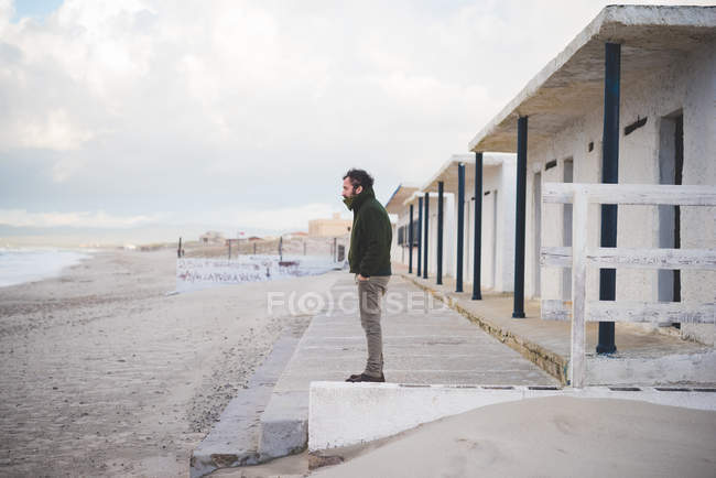 Взрослый мужчина перед пляжными хижинами, Сорсо, Сассари, Сардиния, Италия — стоковое фото