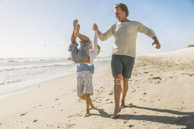 Father and son on beach holding hands, swinging boy — Stock Photo