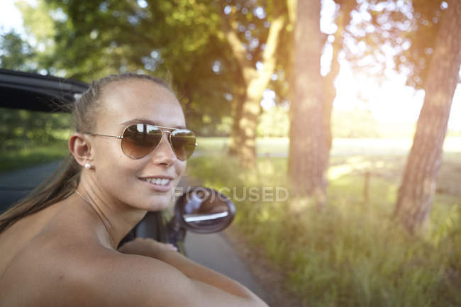 Jovem mulher dirigindo conversível olhando sobre seu ombro — Fotografia de Stock