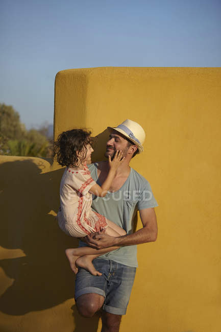 Padre sosteniendo a su hija, apoyado contra la pared, Costa Brava, Cataluña, España - foto de stock