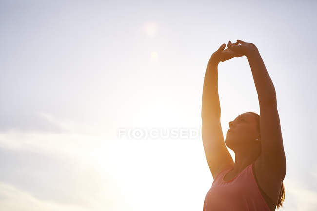 Молода жінка бігунка розтягує руки на сонячне світле небо — стокове фото